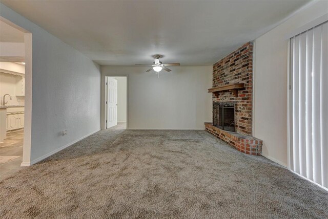 unfurnished living room featuring a sink, ceiling fan, carpet, and a brick fireplace