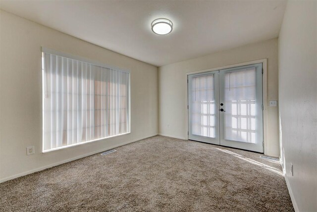 empty room with carpet floors, plenty of natural light, baseboards, and french doors
