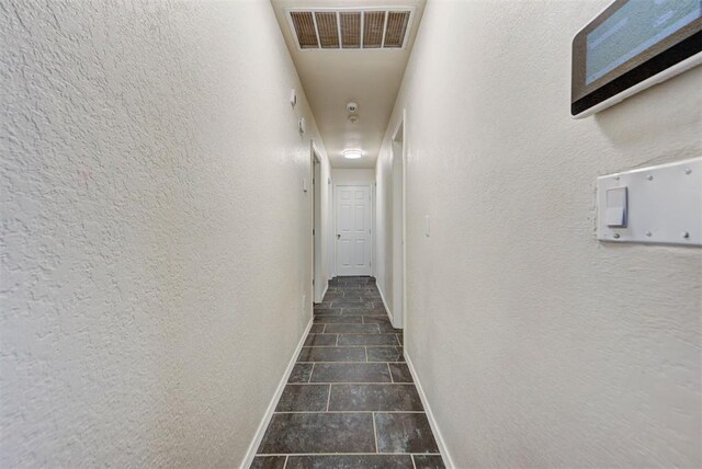 hallway with visible vents, baseboards, a textured wall, and dark tile patterned flooring