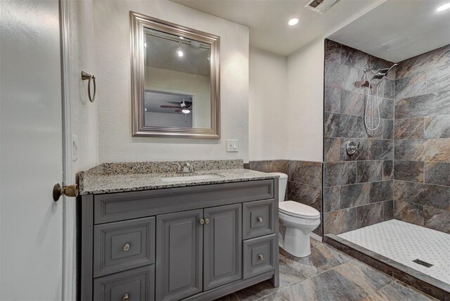 bathroom with vanity, visible vents, toilet, ceiling fan, and tiled shower