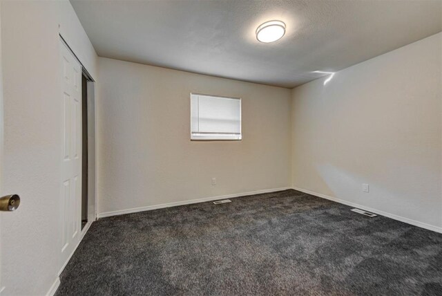 unfurnished bedroom with dark carpet, baseboards, visible vents, and a closet