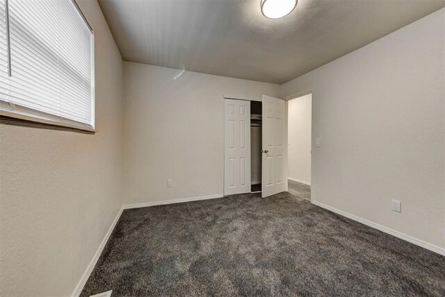 unfurnished bedroom with a closet, baseboards, and dark colored carpet