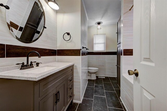 bathroom featuring wainscoting, tile patterned flooring, vanity, toilet, and tile walls