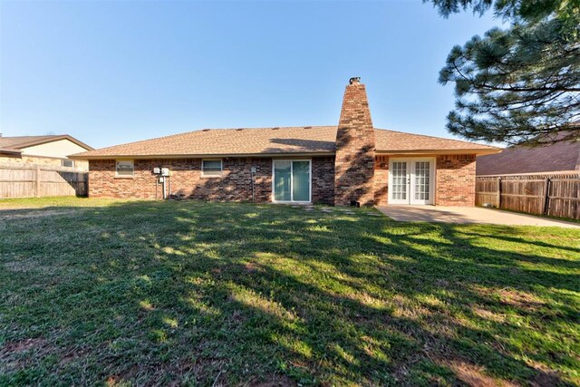 back of property with brick siding, a fenced backyard, a chimney, french doors, and a lawn