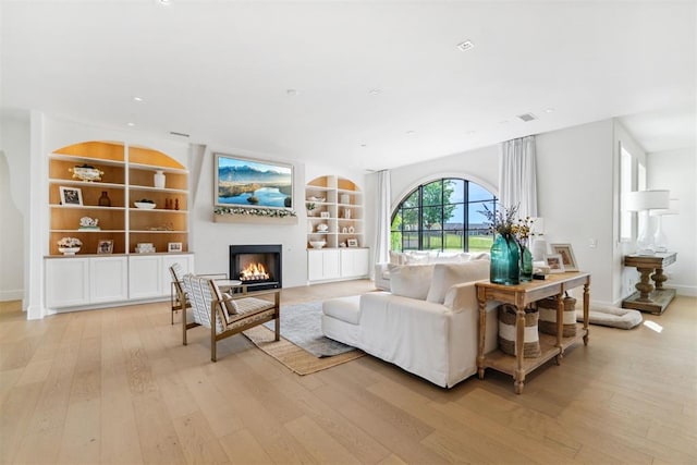 living area featuring built in shelves, baseboards, a lit fireplace, and light wood-type flooring