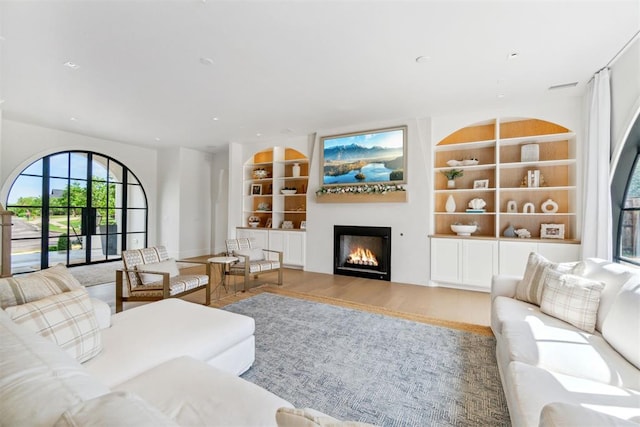 living area with wood finished floors, built in shelves, and a lit fireplace