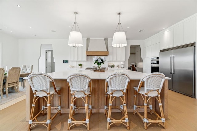 kitchen featuring custom exhaust hood, light wood finished floors, stainless steel appliances, and light countertops