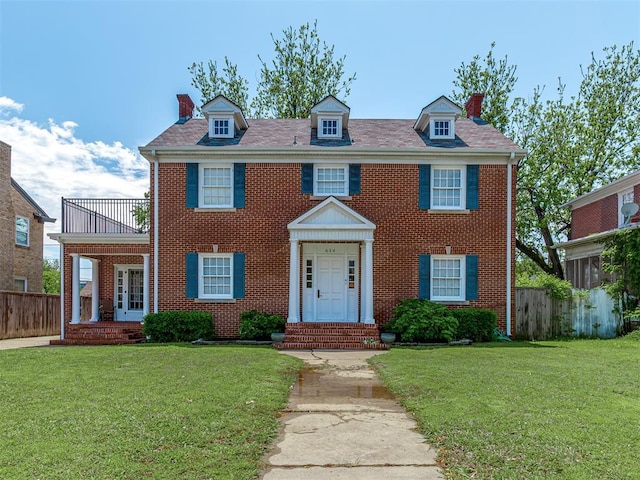 colonial home with a front lawn, fence, brick siding, and a chimney