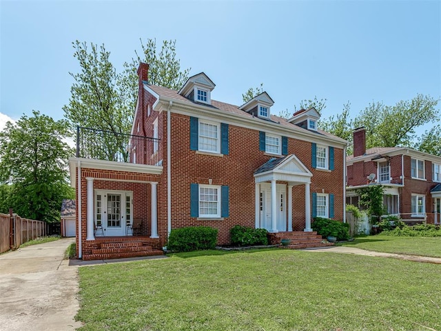 colonial inspired home featuring fence, a front lawn, a chimney, and brick siding
