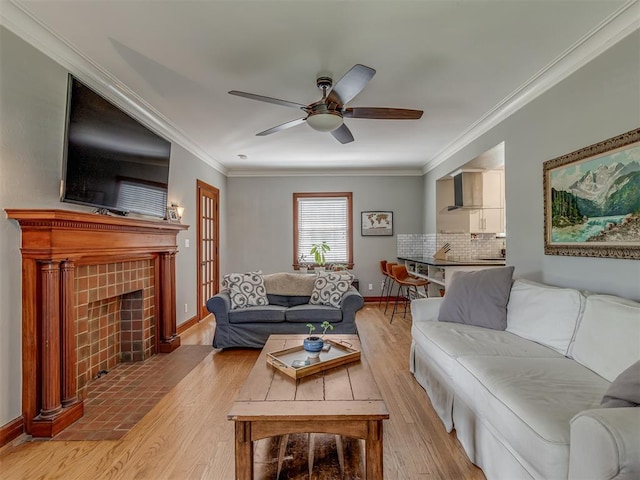 living room with light wood-style flooring, ornamental molding, a fireplace, baseboards, and a ceiling fan