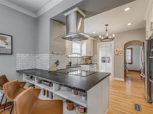 kitchen with open shelves, arched walkways, black electric cooktop, island exhaust hood, and a peninsula