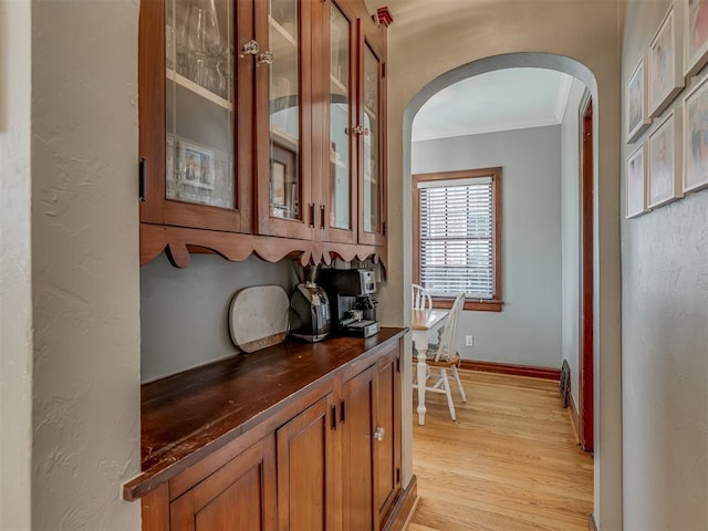 interior space featuring ornamental molding, light wood finished floors, arched walkways, and baseboards