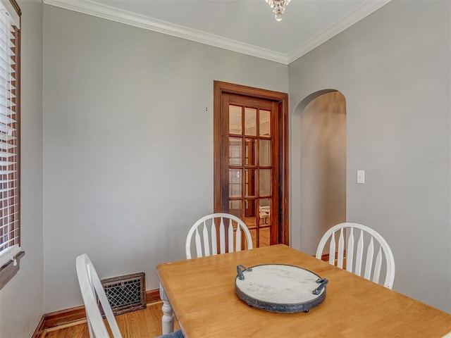 dining room featuring wood finished floors, arched walkways, baseboards, visible vents, and crown molding