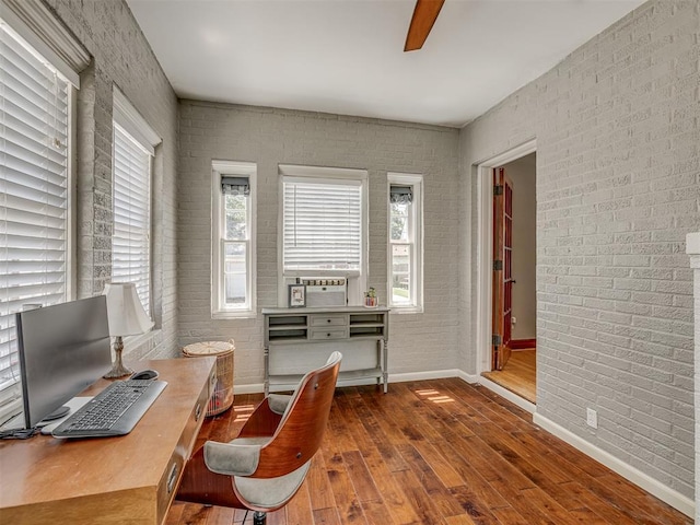 office space featuring a ceiling fan, brick wall, wood finished floors, and baseboards
