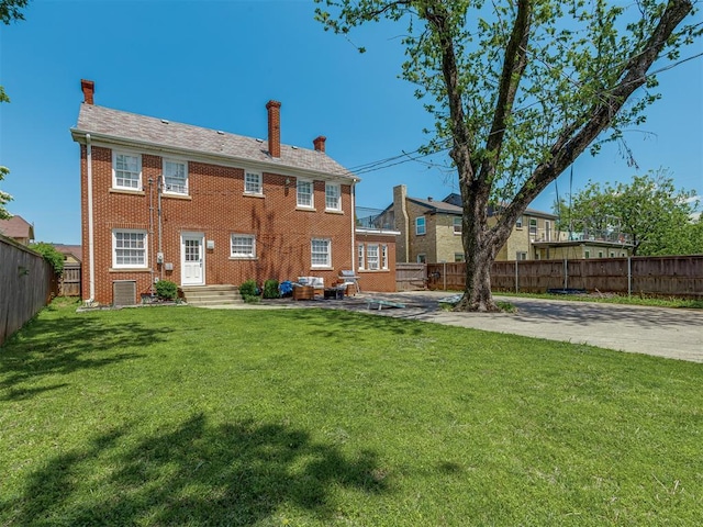 rear view of property featuring brick siding, a yard, a fenced backyard, and a chimney
