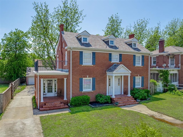 colonial house featuring driveway, a balcony, a chimney, a front lawn, and brick siding