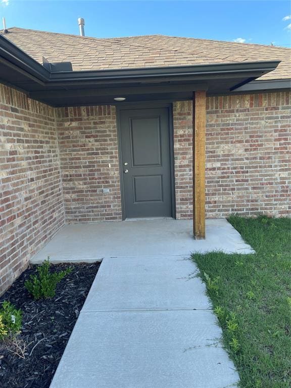property entrance featuring brick siding and a shingled roof