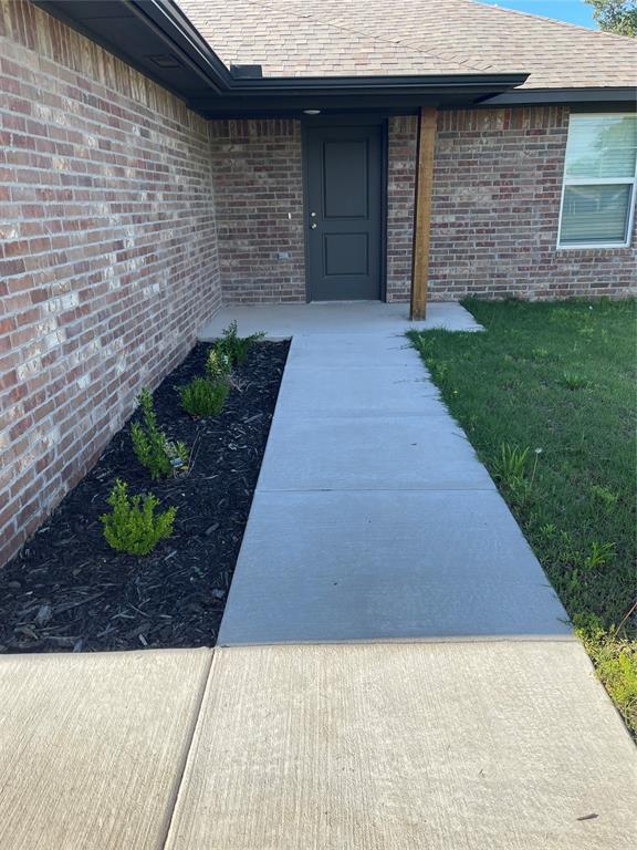 doorway to property featuring roof with shingles and brick siding