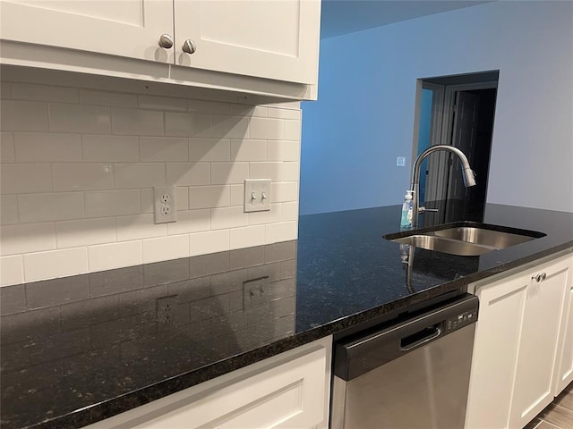kitchen with stainless steel dishwasher, dark stone counters, white cabinets, a sink, and backsplash