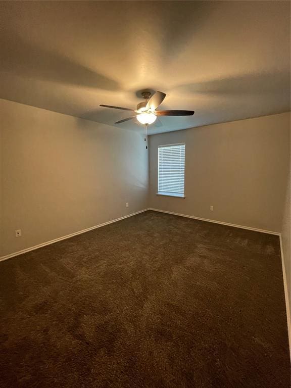 empty room featuring dark colored carpet, a ceiling fan, and baseboards