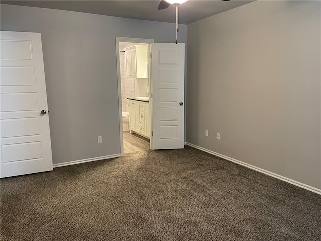 unfurnished bedroom featuring dark carpet, baseboards, and ensuite bathroom