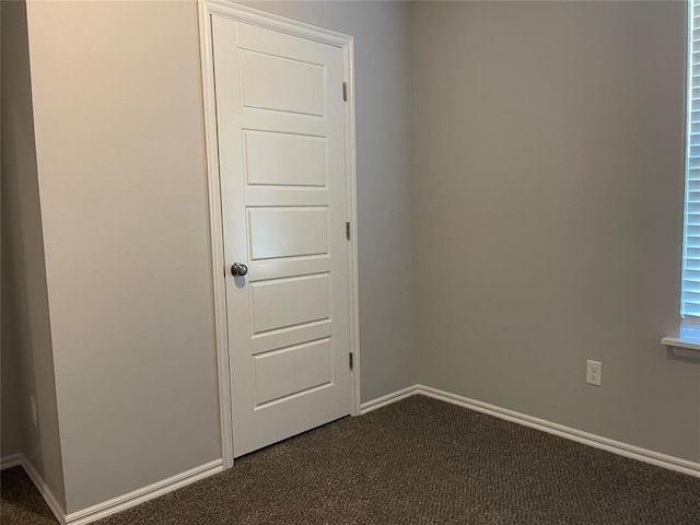unfurnished room with baseboards and dark carpet