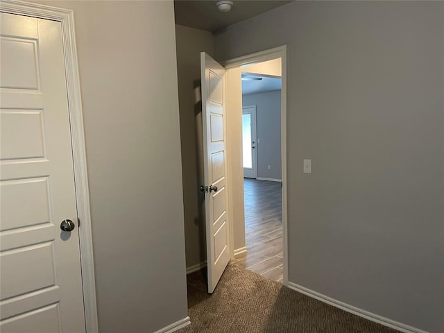corridor featuring baseboards and dark carpet