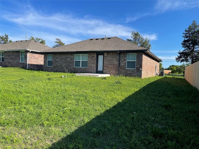 rear view of property featuring a lawn, brick siding, a shingled roof, and central air condition unit