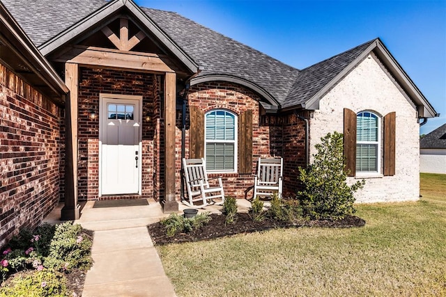 doorway to property featuring brick siding, a shingled roof, and a lawn