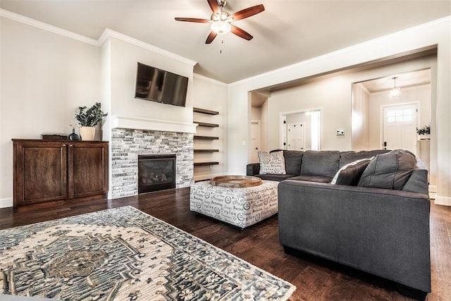 living area with wood finished floors, ornamental molding, ceiling fan, a stone fireplace, and baseboards