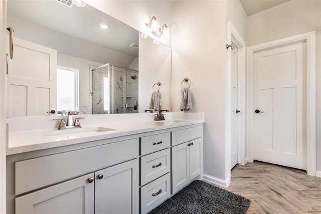 bathroom with baseboards, a shower stall, double vanity, and a sink