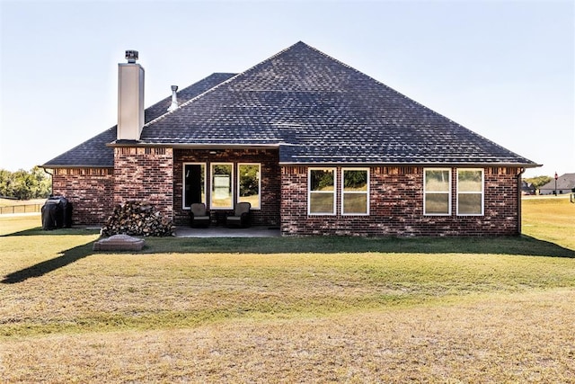 rear view of house featuring a chimney, a yard, brick siding, a patio, and roof with shingles