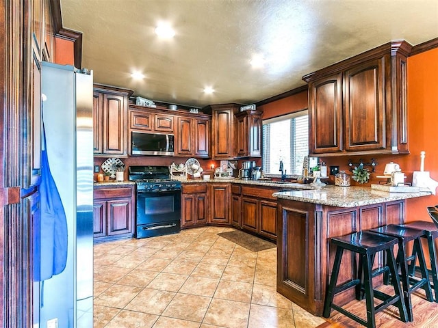 kitchen with a peninsula, a breakfast bar area, light stone counters, a sink, and stainless steel appliances