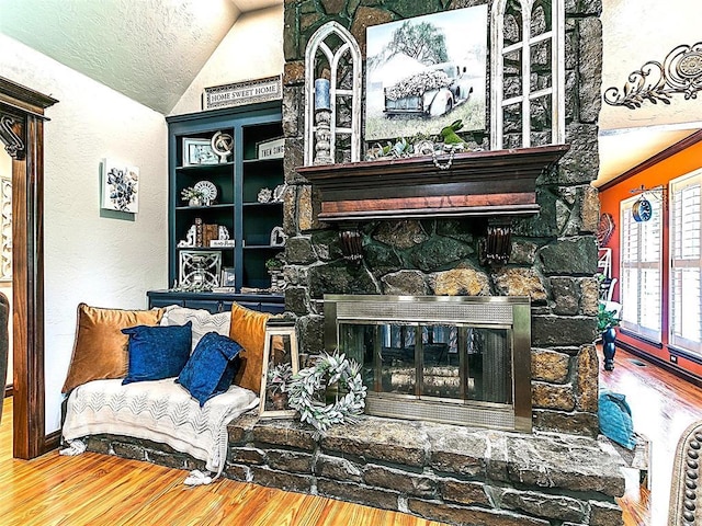 sitting room featuring a textured wall, vaulted ceiling, wood finished floors, and a fireplace