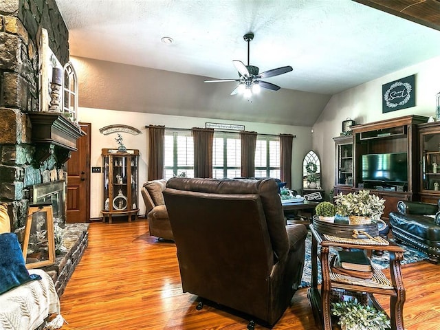 living area featuring a ceiling fan, a textured ceiling, a fireplace, wood finished floors, and lofted ceiling