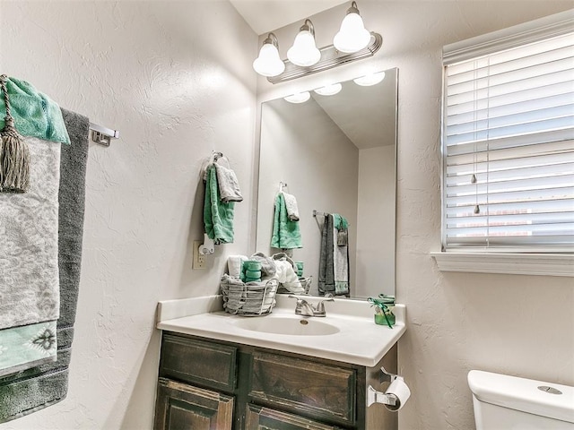 half bath featuring vanity, a textured wall, and toilet
