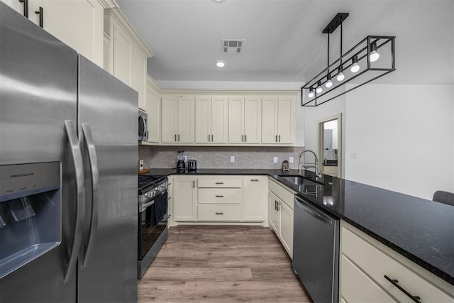 kitchen with wood finished floors, decorative backsplash, stainless steel appliances, a sink, and visible vents
