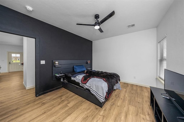 bedroom with a ceiling fan, visible vents, wood finished floors, and baseboards