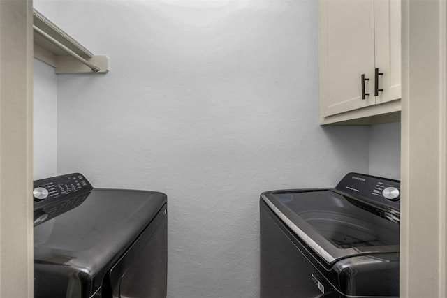 washroom featuring washing machine and dryer, cabinet space, and a textured wall