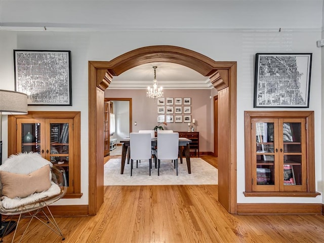 dining area with a notable chandelier, arched walkways, baseboards, light wood-type flooring, and ornamental molding