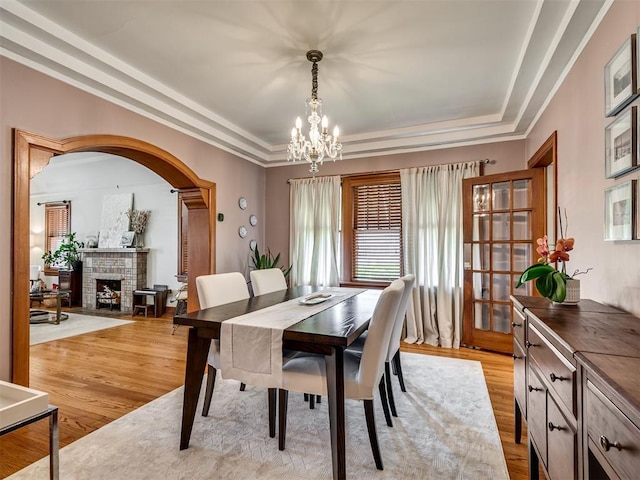 dining area featuring arched walkways, a fireplace, a notable chandelier, a tray ceiling, and light wood-style flooring