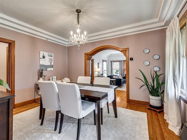 dining space featuring an inviting chandelier, a raised ceiling, light wood finished floors, and arched walkways
