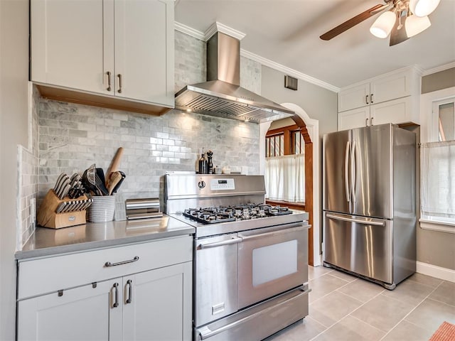 kitchen featuring wall chimney range hood, stainless steel appliances, a ceiling fan, and tasteful backsplash