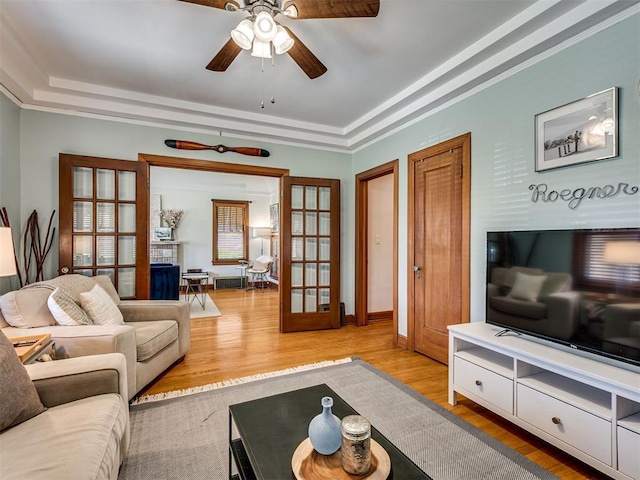 living area with a raised ceiling, a ceiling fan, french doors, and wood finished floors