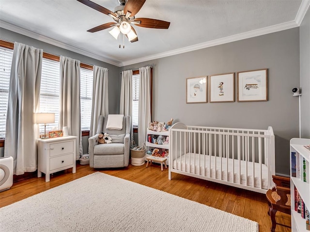 bedroom featuring ornamental molding, a crib, ceiling fan, and wood finished floors