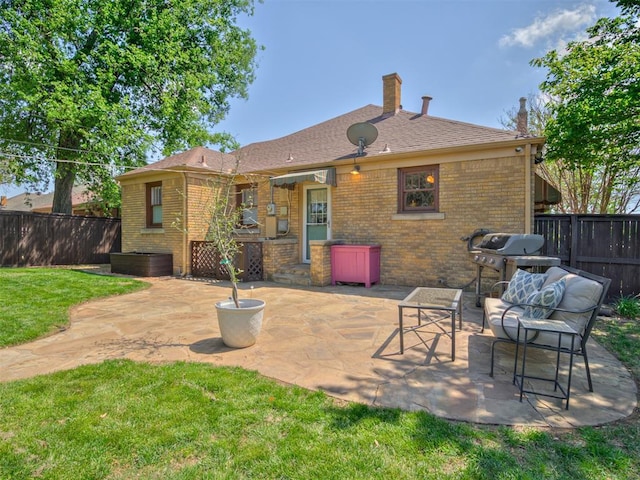 back of house with a chimney, a lawn, brick siding, a fenced backyard, and a patio