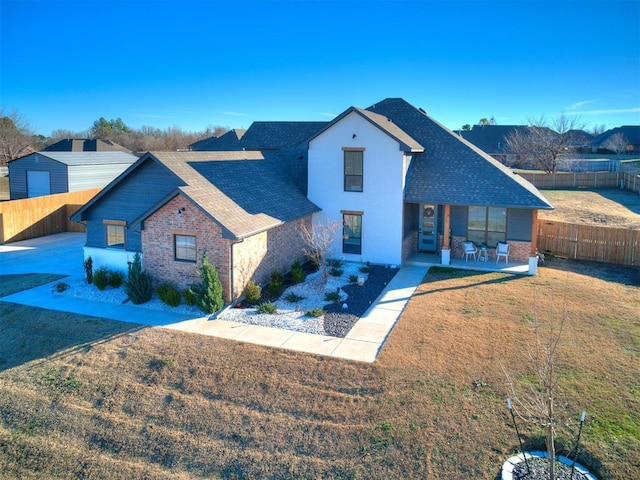 view of front of home with brick siding, a fenced backyard, and roof with shingles