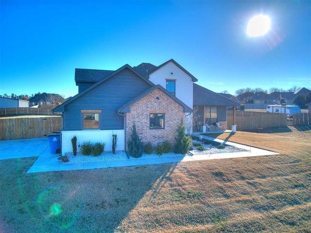 view of front of house featuring brick siding, a front lawn, a patio area, and fence