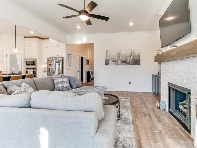 living room with ceiling fan, a fireplace, light wood-type flooring, ornamental molding, and recessed lighting