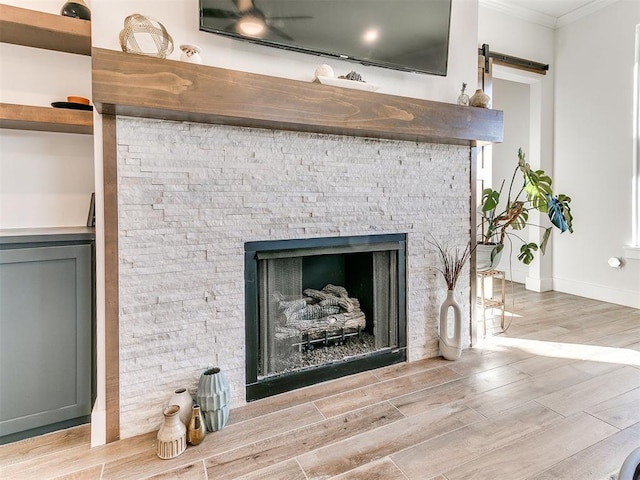 interior details with a fireplace, a barn door, wood finished floors, baseboards, and ornamental molding